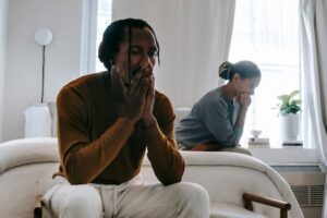 Wistful concerned African American couple in casual clothing sitting on bed at home after having quarrel