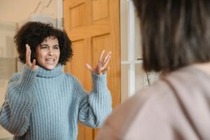 Angry young multiracial ladies in casual clothes standing in bright apartment near door while having disagreement and looking at each other